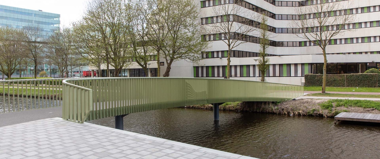 mosgroene fietsbrug met spijlenhekwerk en afbeelding Atlastgebouw dat ook op de achtergrond staat